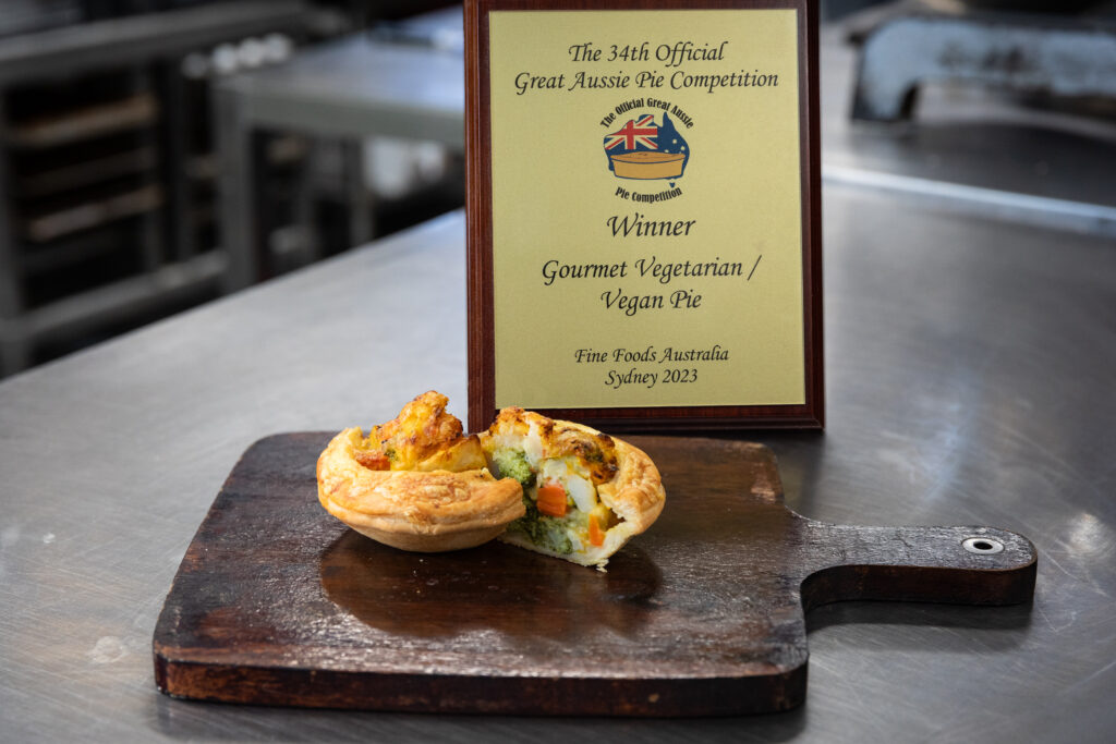 A vegetarian pie cut in half to show its vegetable insides in front of an award for Gourmet Vegetarian Vegan Pie category at the 2023 Great Aussie Pie Competition